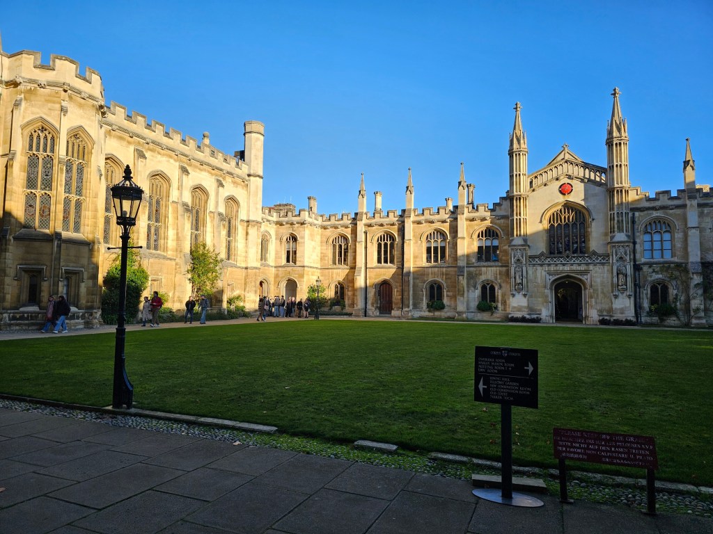 A square patio of a college house in Cambridge, England. There's a low rise stone building running around a green lawn.