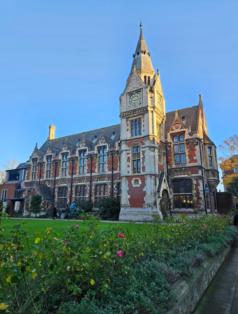 A square patio of a college house in Cambridge, England. There's a stone chapel, a green lawn and a handful of flowers.
