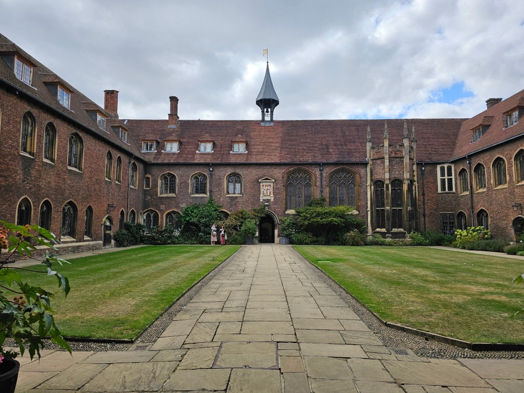 A square patio of a college house in Cambridge, England. There's a low rise stone building running around a green lawn.