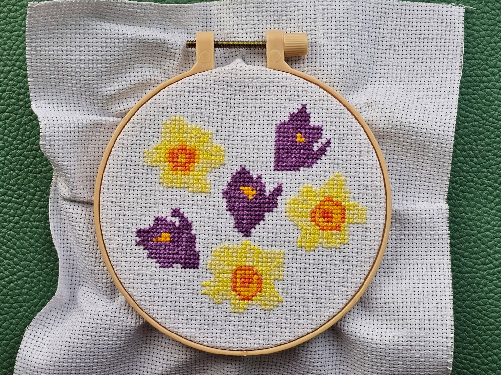 Partly completed cross stitch project featuring daffodils and crocuses. Green leaves are missing.