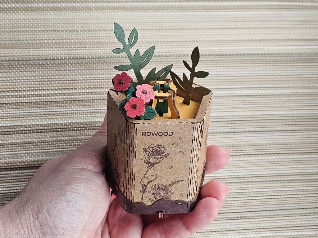 Assembled wooden and cardboard stand for 3D wooden flowers. There are miniature wooden flowers adorning the stand.