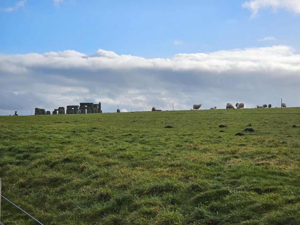 The Stone Circle in Stonehenge seen in the distance, and some grazing sheep on the cast meadows.