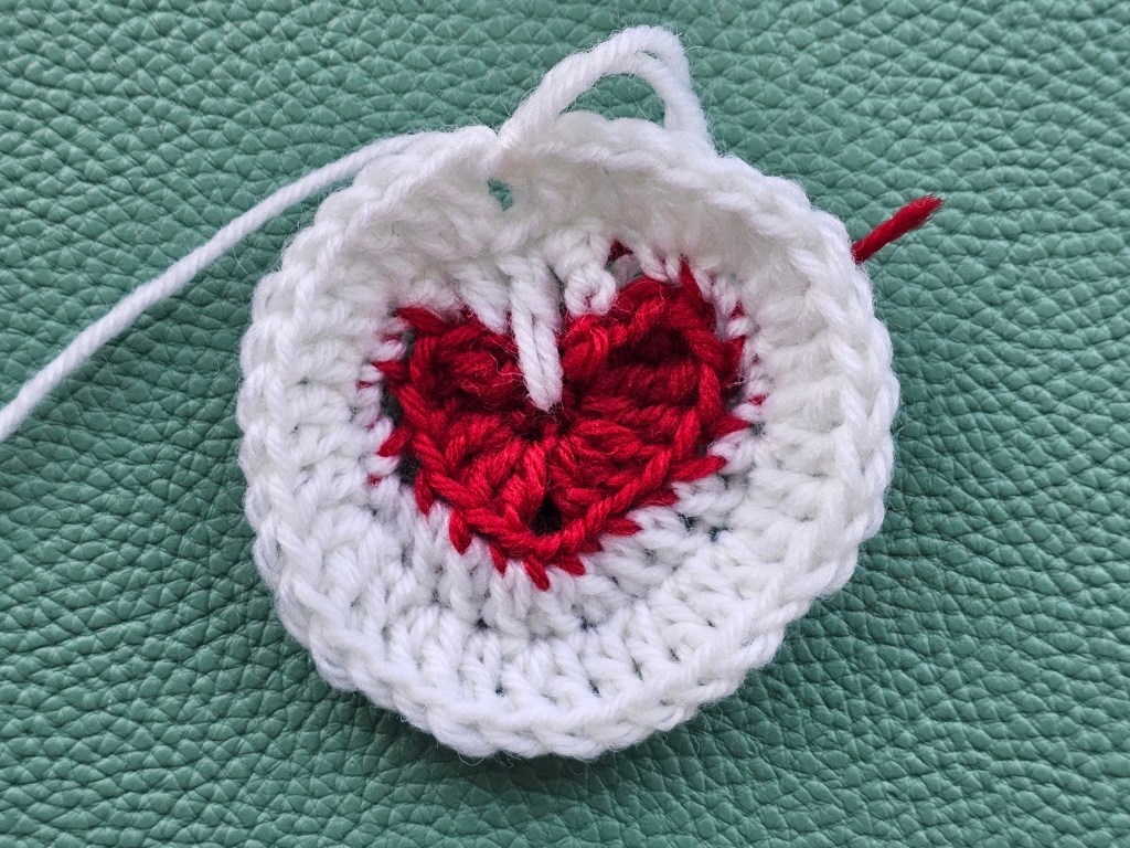 Partially completed crocheted coasters - a white circle with a red heart in the middle