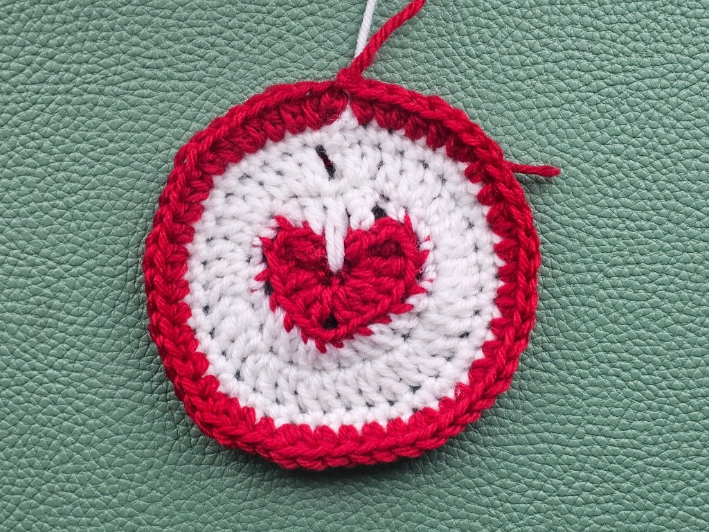 Partially completed crocheted coaster with a heart in the middle