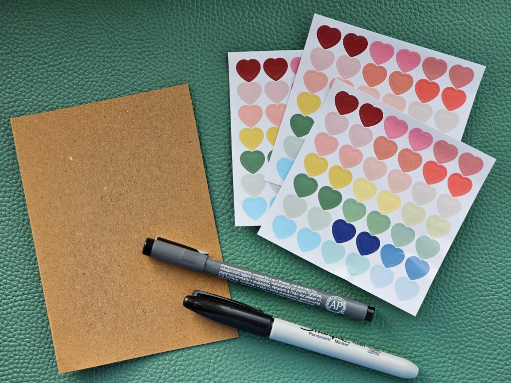 A blank card made of brown paper, sheets of heart shaped stickers, and black marker pens