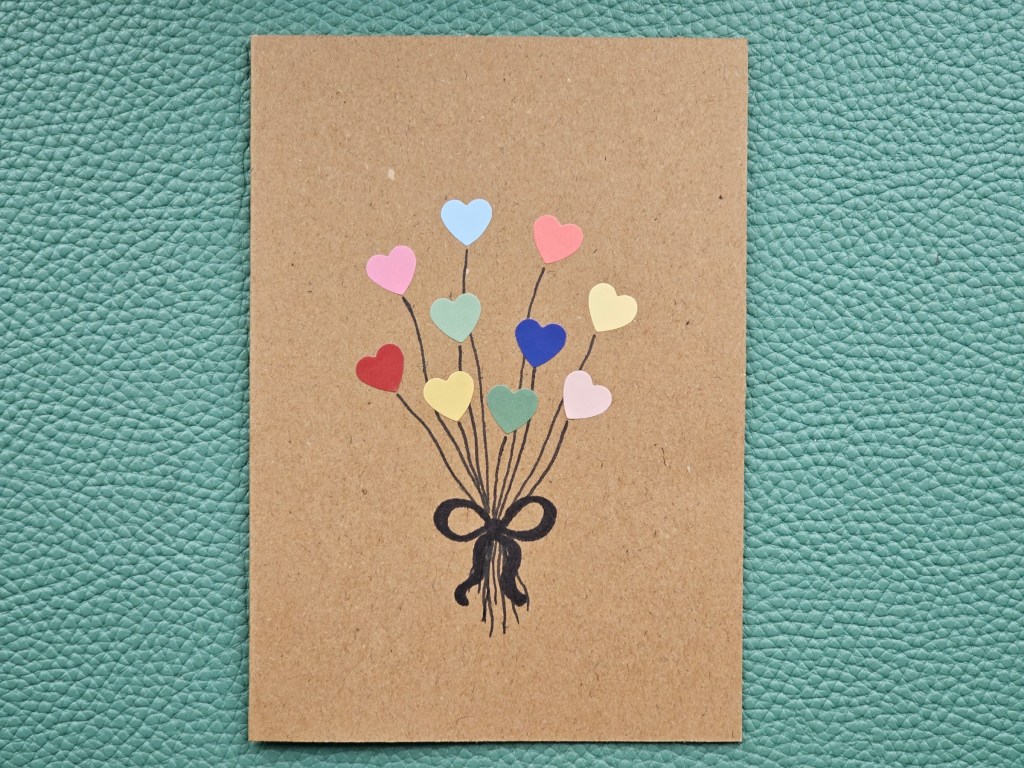 Finished DIY Valentine's Day card featuring a bunch of hearts on strings, tied with a bow