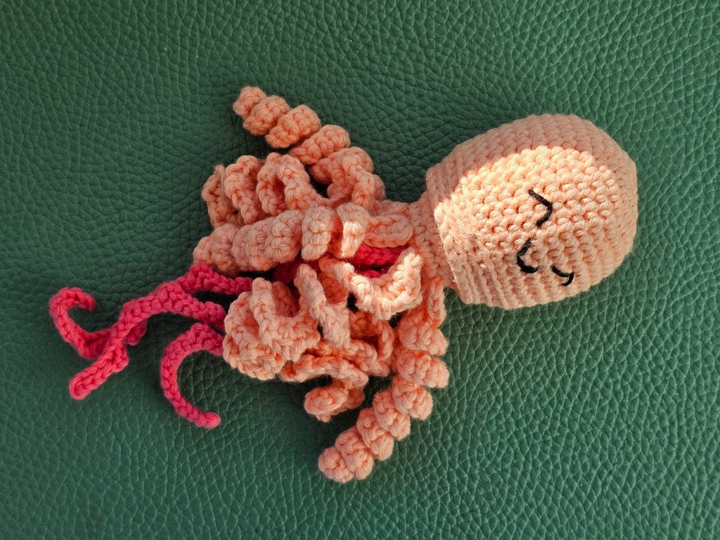 Nearly completed crocheted jellyfish in peach and pink colour