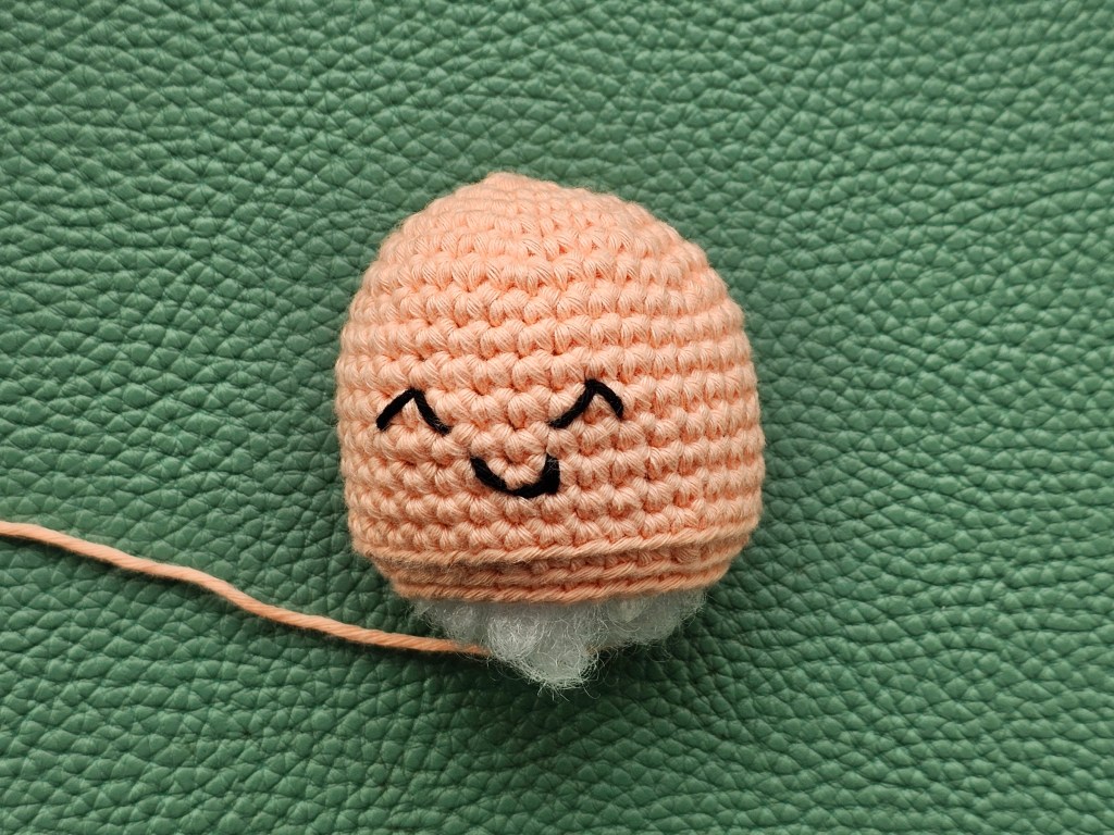 Crocheted unfinished head / body of a jellyfish with embroidered face details and toy stuffing sticking out