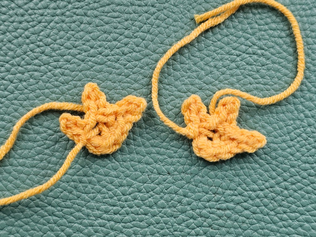 Two small crocheted orange chicken feet with three toes