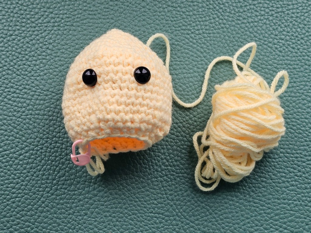 Yellow crocheted head of a chicken with safety eyes attached