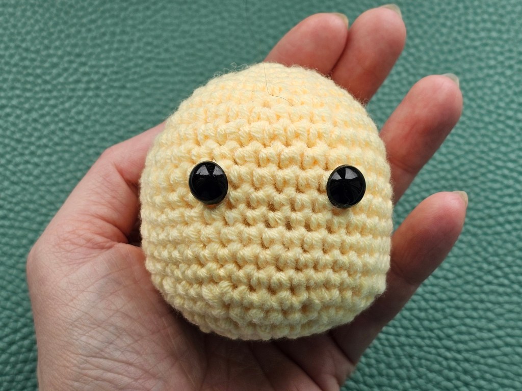 Yellow crocheted head of a chicken with safety eyes attached