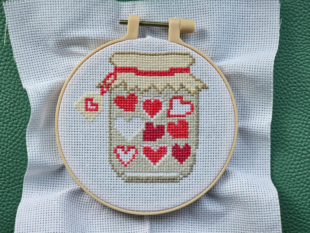 Nearly completed cross stitch project featuring a jar of hearts.