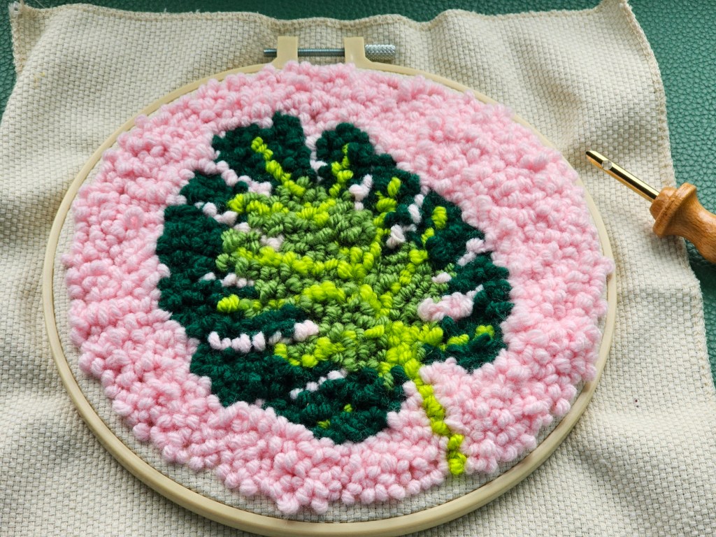 Finished round punch needle canvas featuring a monstera leaf on a pink background