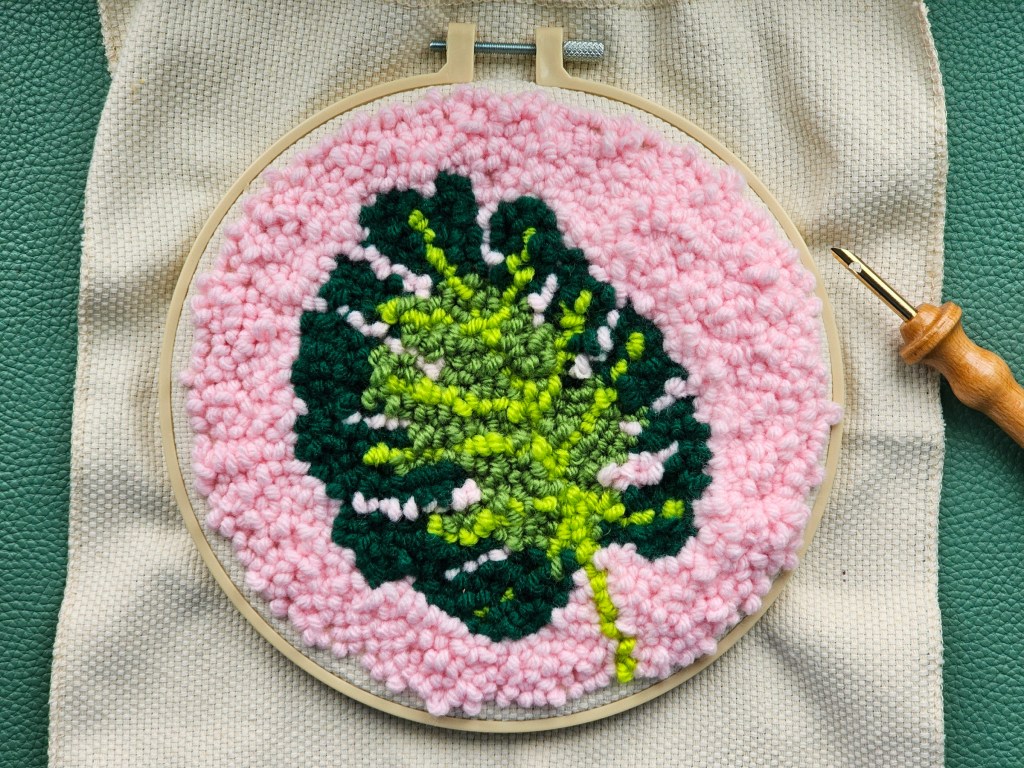 Finished round punch needle canvas featuring a monstera leaf on a pink background
