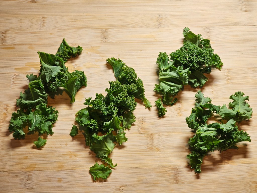 Pieces of kale on a wooden board, stems removed.