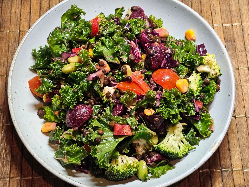 A plate with a generous serving of a salad made with kale, beetroot, tomatoes, corn, broccoli and lentils