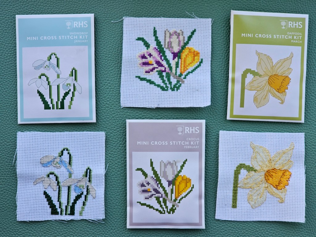 Three completed mini cross stitch designs featuring flowers: snowdrops, crocuses and a daffodil