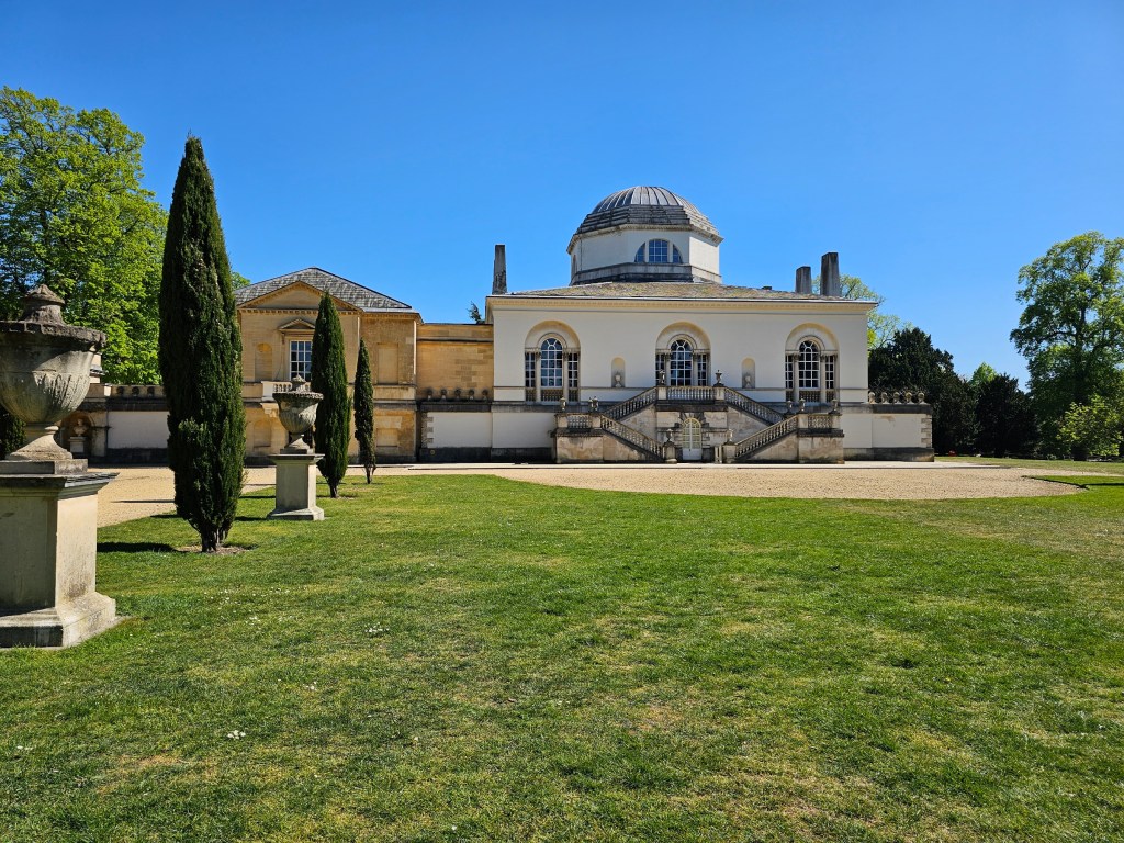 Chiswick House, London. Photo taken from the back. There is green grass and blue skies.
