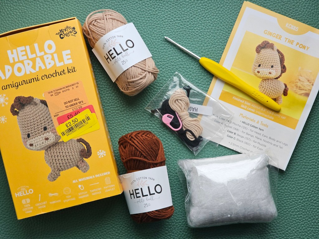 Contents of a crochet kit for making a pony. It includes yarn, a crochet hook, toy filling, a needle and a stitch marker