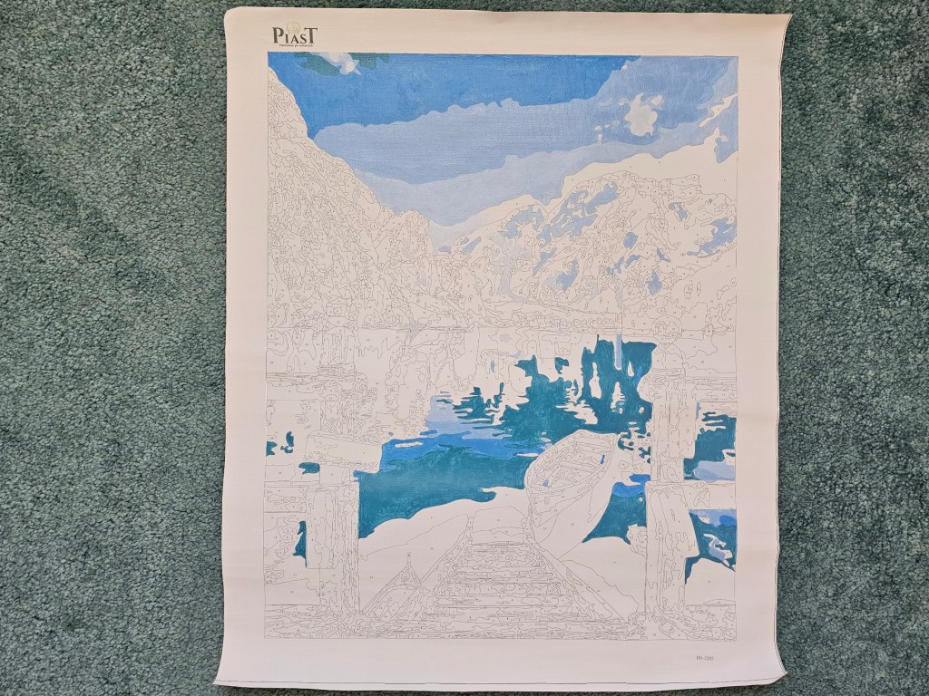 Partially completed painting by numbers project depicting a lake in the mountains.