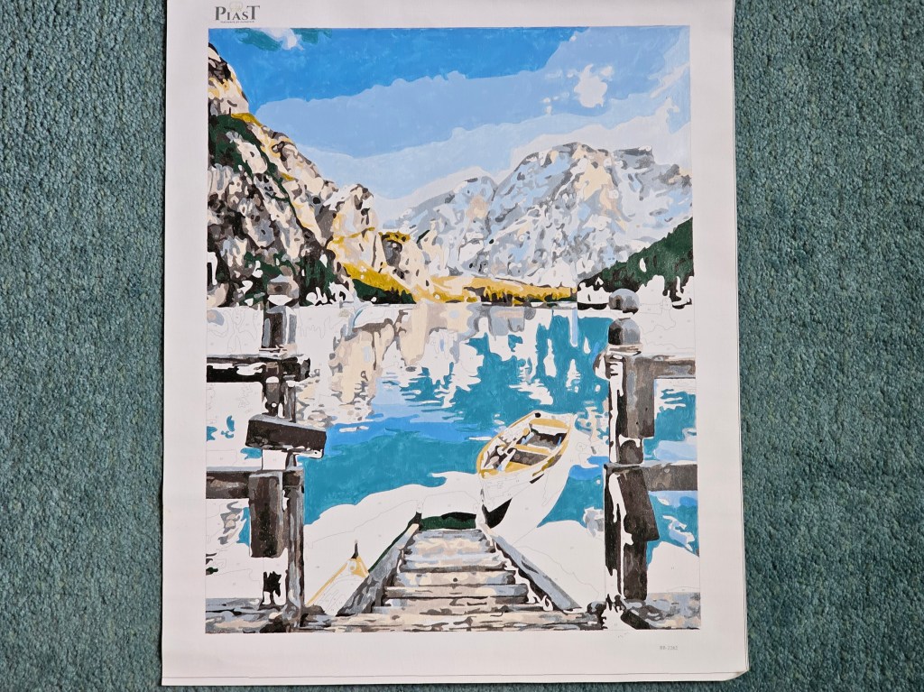 Nearly finished painting by numbers project depicting a lake in the mountains.