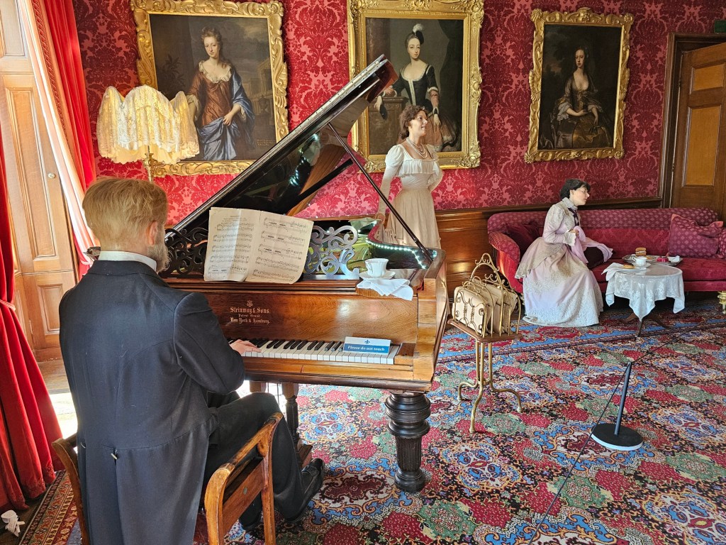 State rooms of Warwick Castle, England, with realistic figures of aristocrats, including a pianist and a lady sitting on a sofa