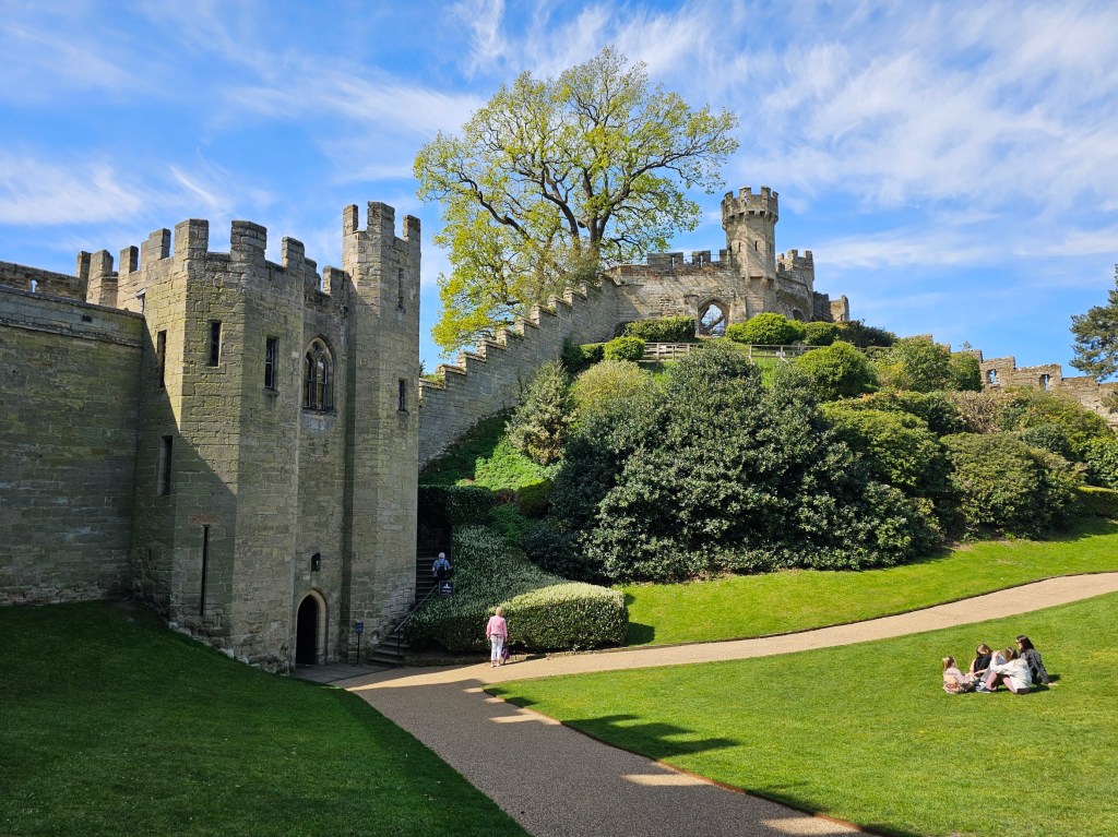 The mound of Warwick Castle, England. There are castle walls climbing up a small hill.