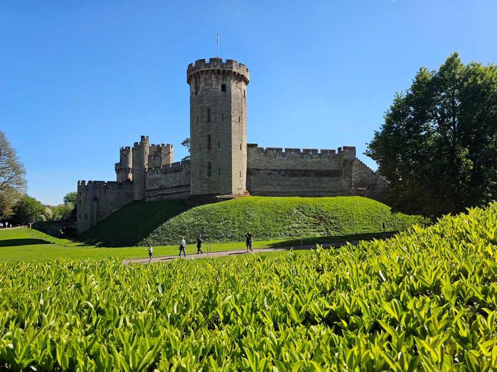 Warwick Castle, England, seen from the outside. There's completely blue sky and green grass.