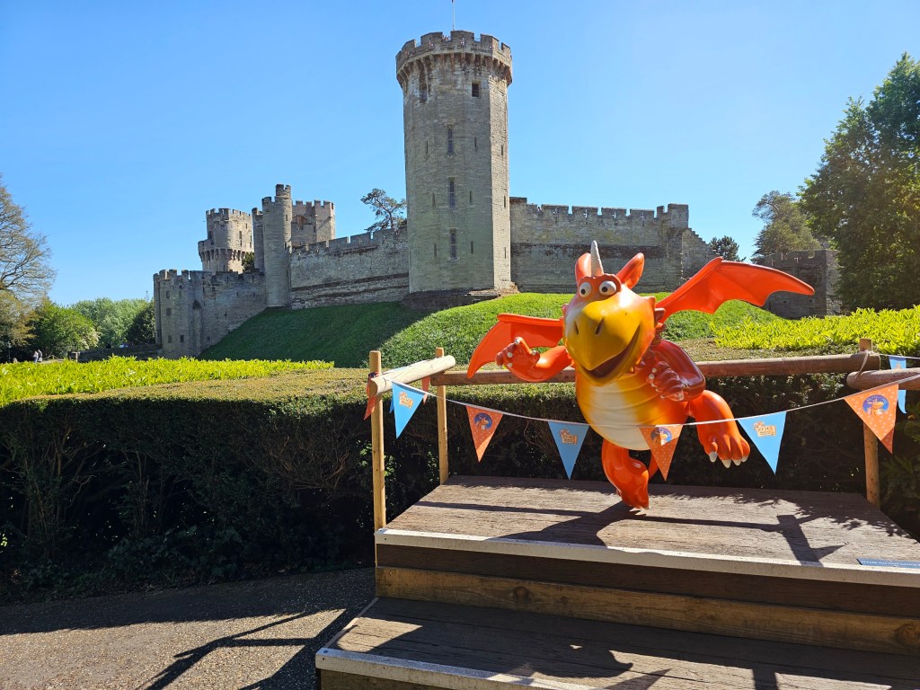 A statue of a cartoon-looking orange dragon named Zog, in front of Warwick Castle, England
