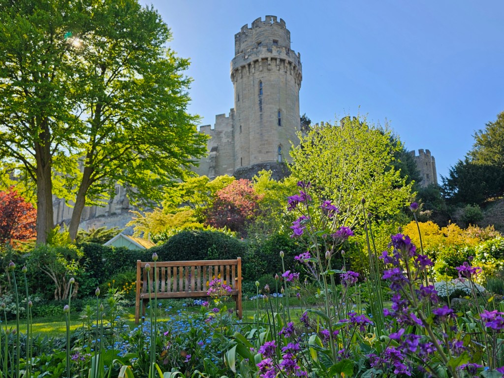 Warwick Castle seen from the Mill Garden There is green grass and colourful flowers