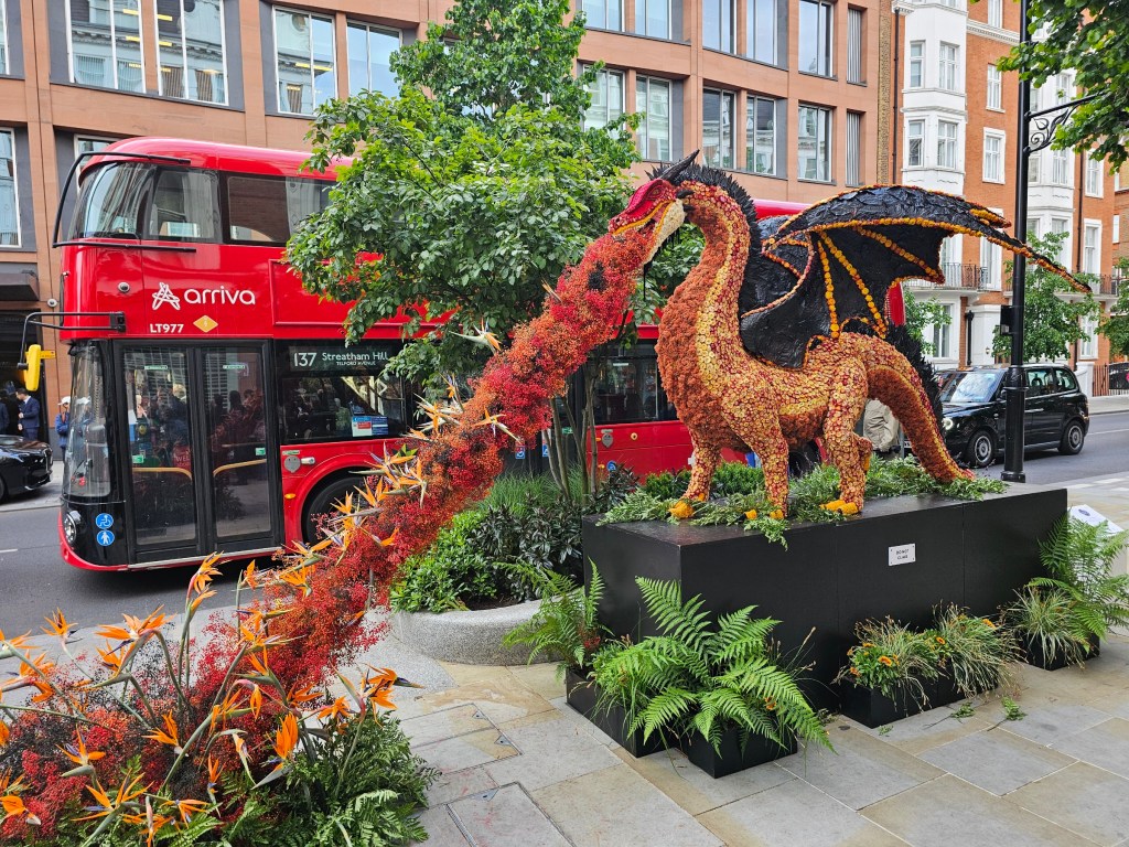 A large statue of a dragon breathing fire, made out of flowers. Photo taken during Chelsea in Bloom event in London in 2026