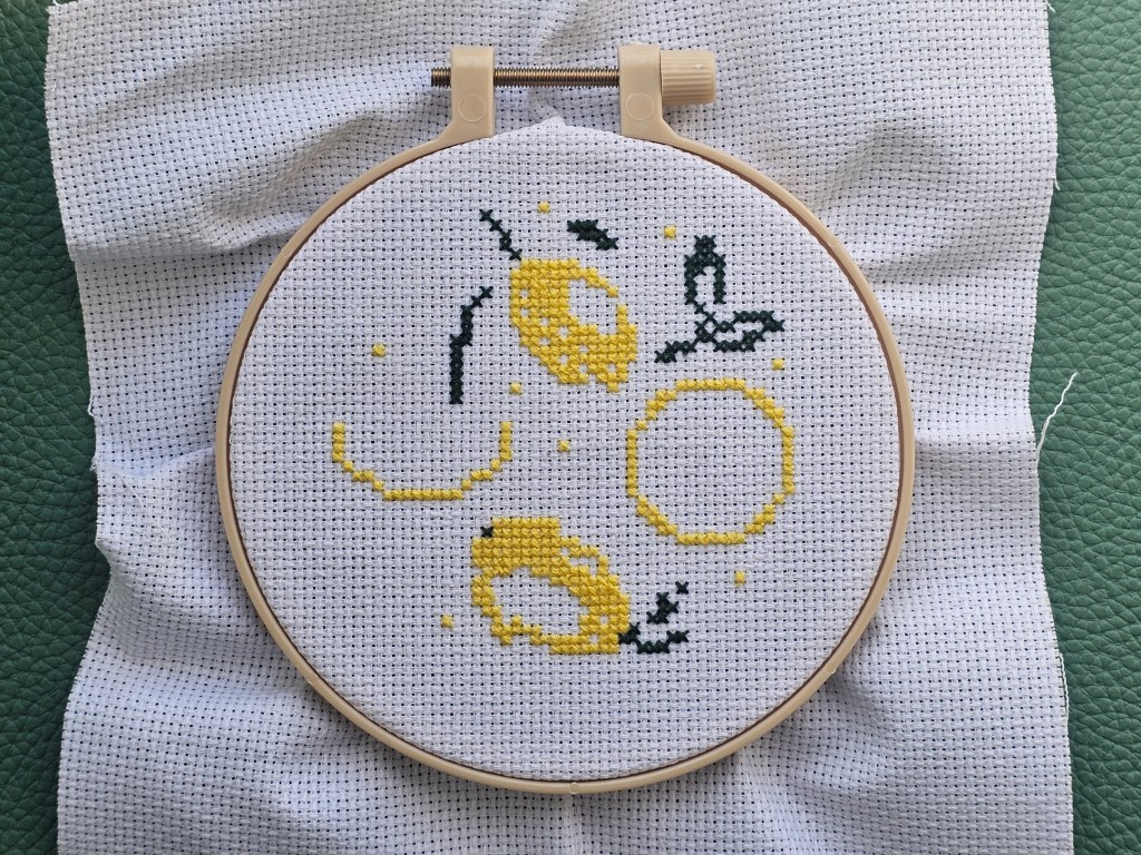Partially finished cross stitch project with a lemon design. The dark yellow and dark green elements are finished
