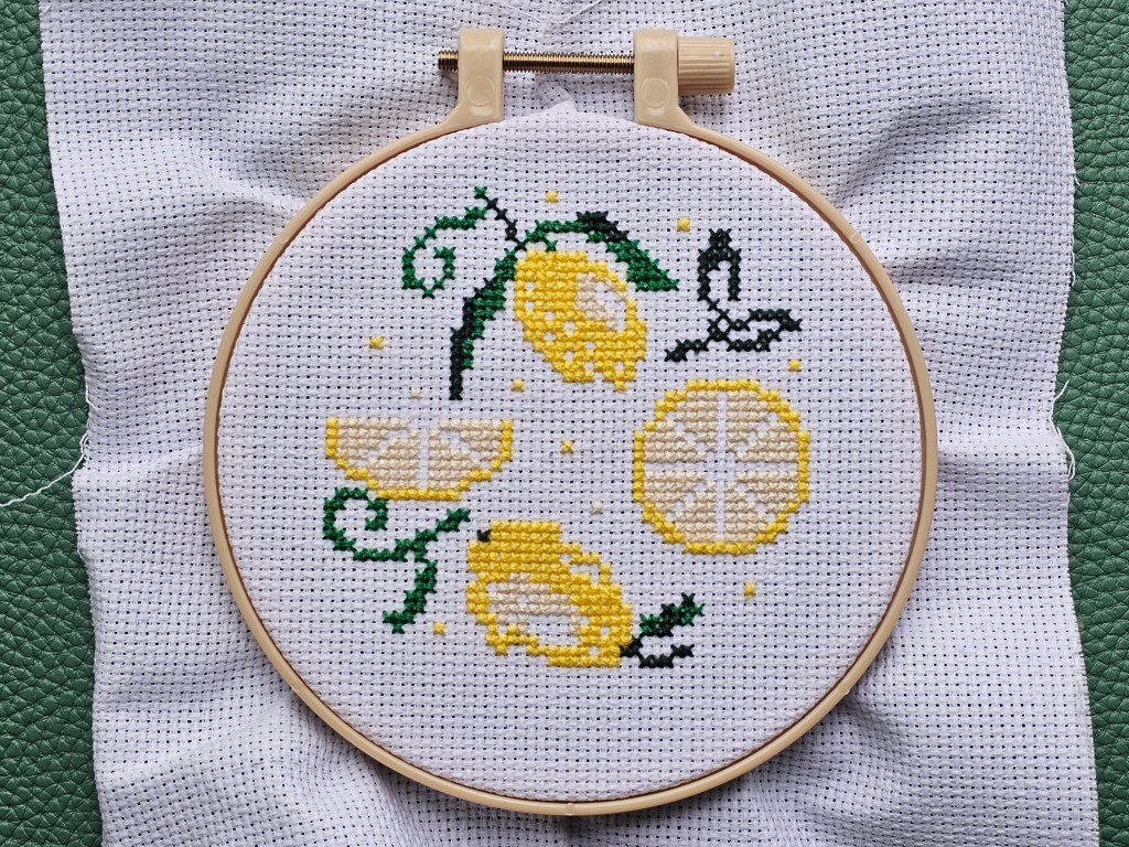 Partially finished cross stitch project with a lemon design. The yellow and dark green elements are finished