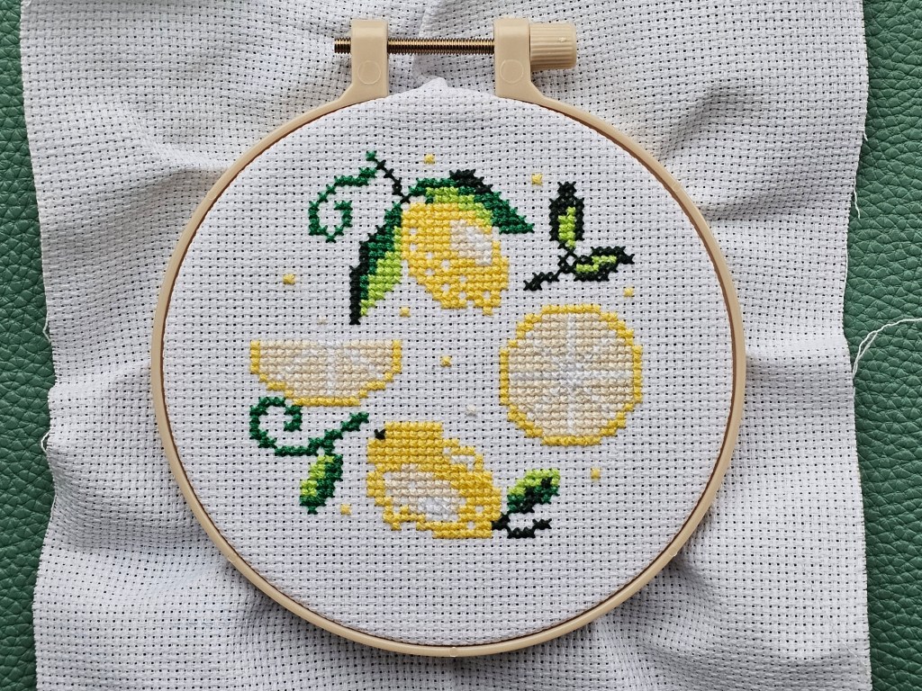 Partially finished cross stitch project with a lemon design. The yellow and green elements are finished