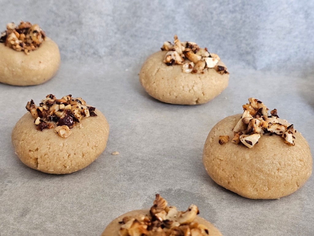 Round pieces of cookie dough topped with honey roasted nuts, on a baking tray
