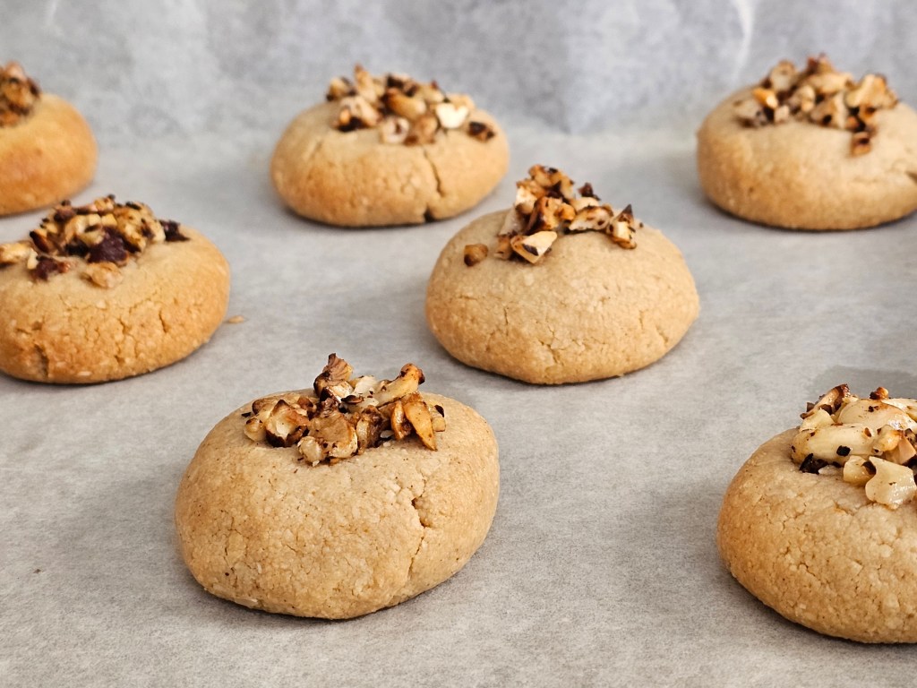 Baked tahini almond cookies topped with honey roasted nuts, on a baking tray