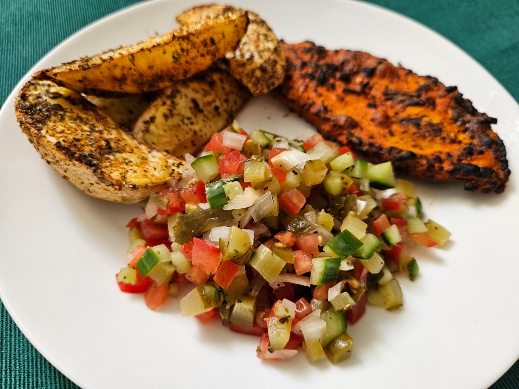 Salad with tomatoes, cucumber and onion on a plate with grilled chicken and roasted potatoes