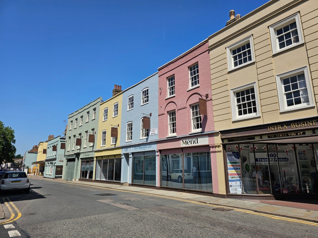 A row of low rise buildings painted in pastel colours: sage, yellow, blue, and pink