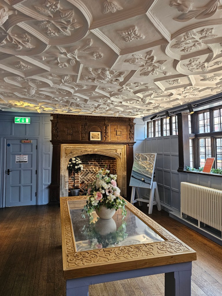 A room inside Eastgate House, with the walls painted in pale blue and the ceiling decorated with carved panels