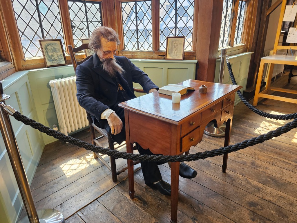 A realistic figure of Charles Dickens sitting at his desk, recreated from a real photo of the writer