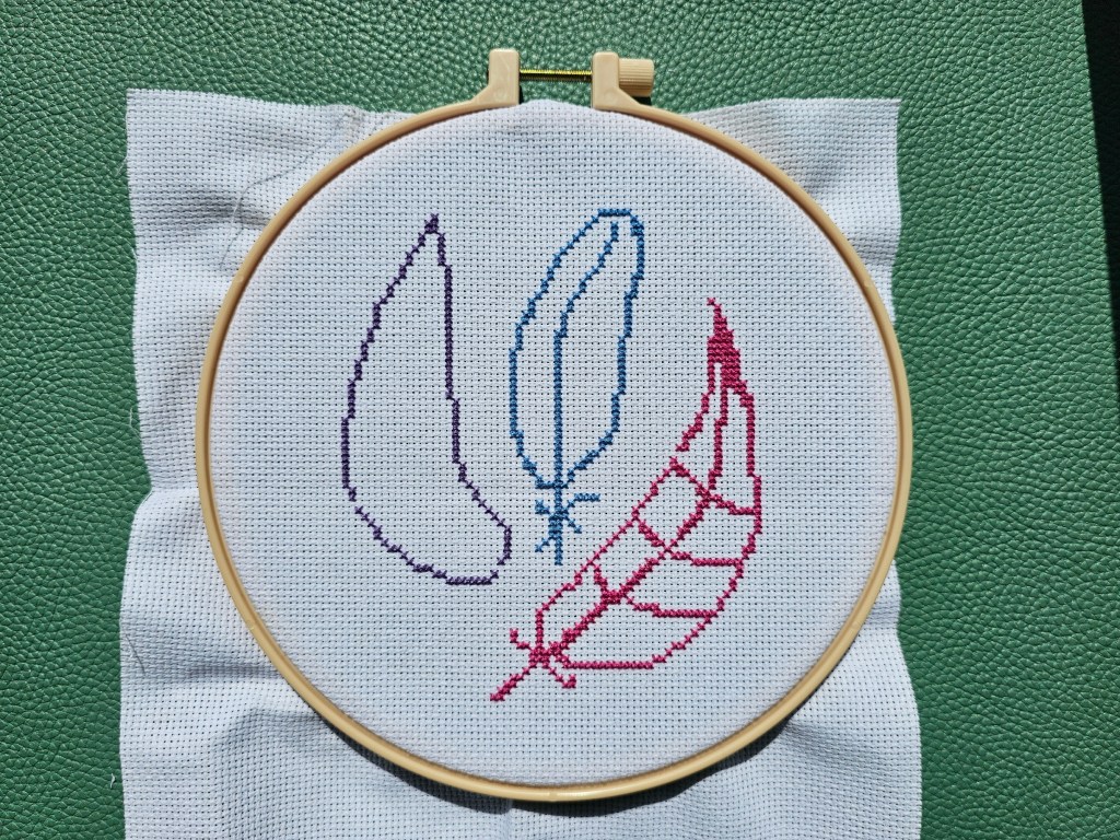 Outlines of three cross stitched feathers on a canvas, in purple, blue and pink.