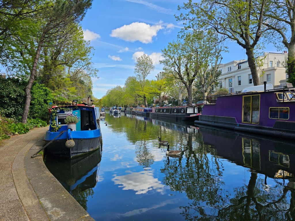 A canal with several narrowboats along a footpath in London