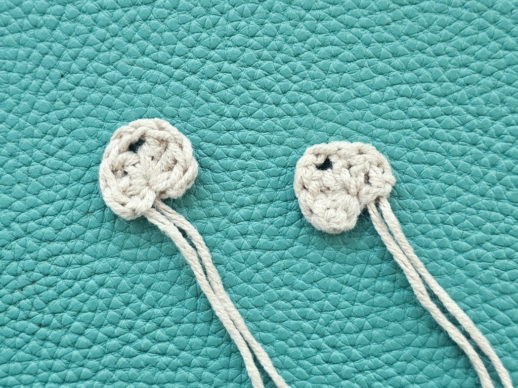 Two crocheted tiny beige heart-shaped elements that will become ears of an owl