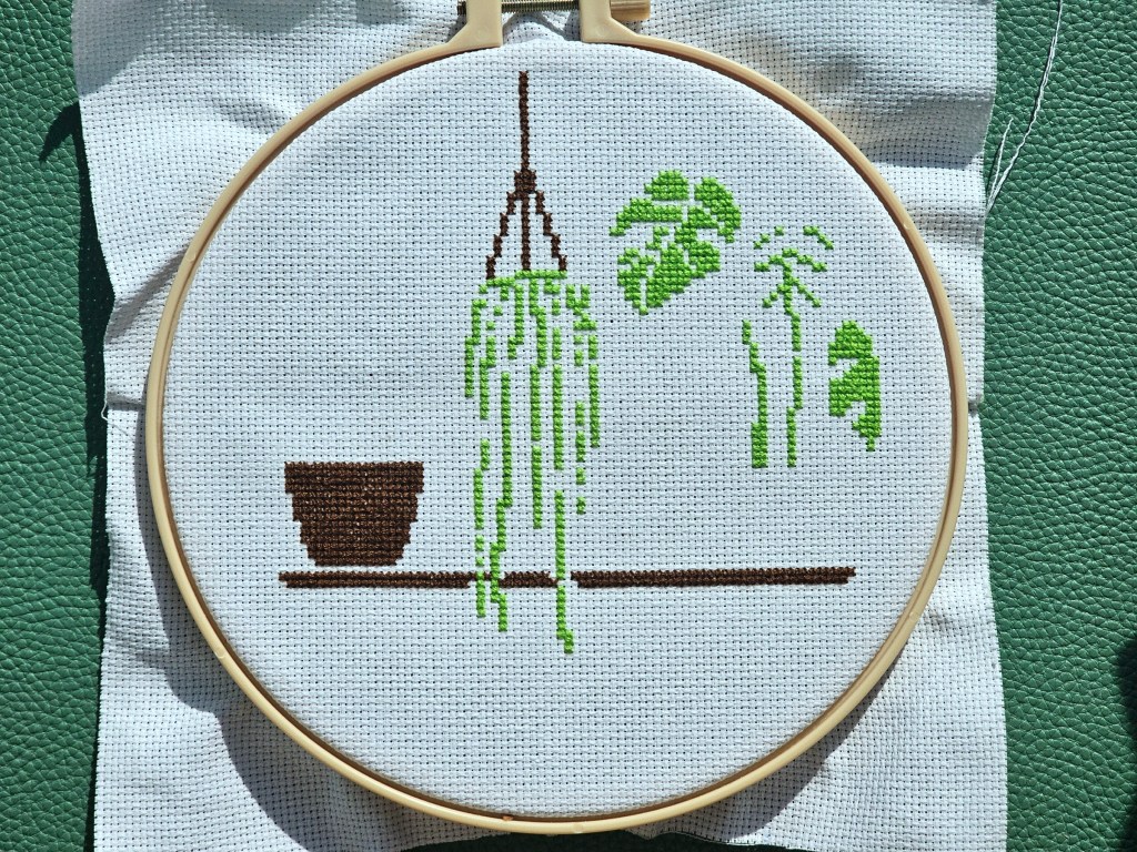 The first elements of a cross stitch project featuring house plants on a shelf