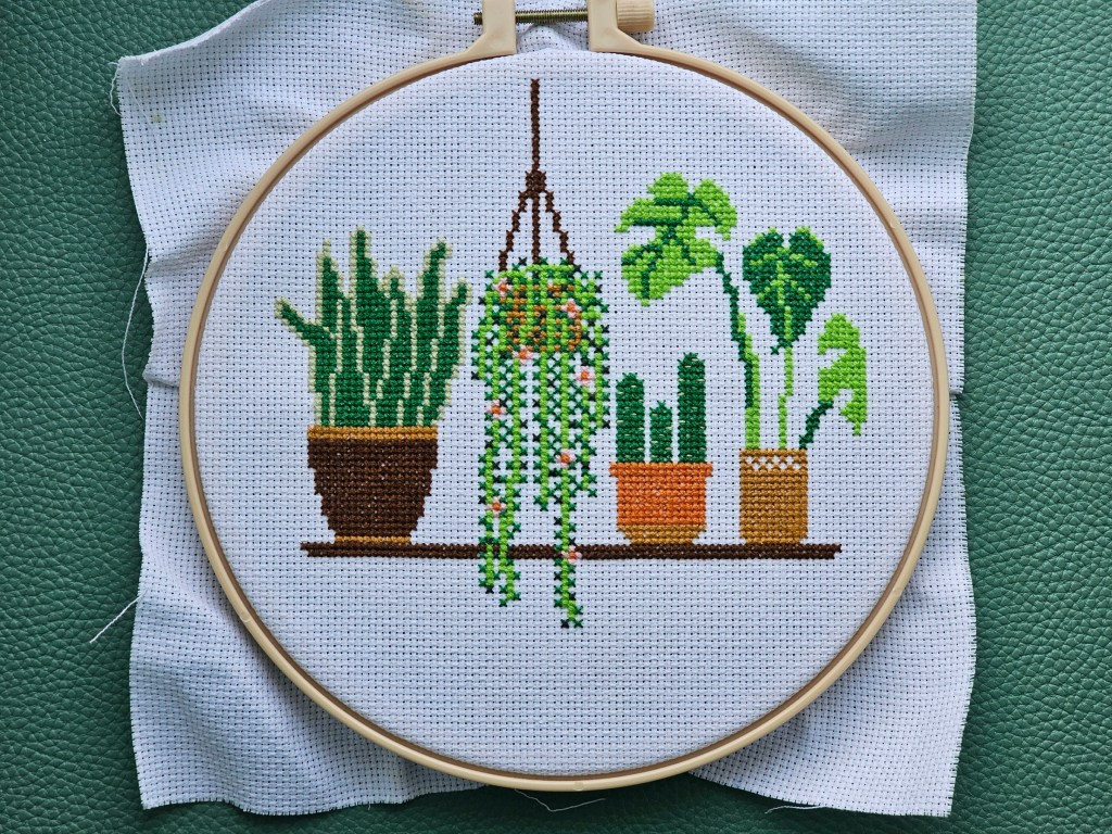 Completed cross stitch project featuring four house plants on a shelf
