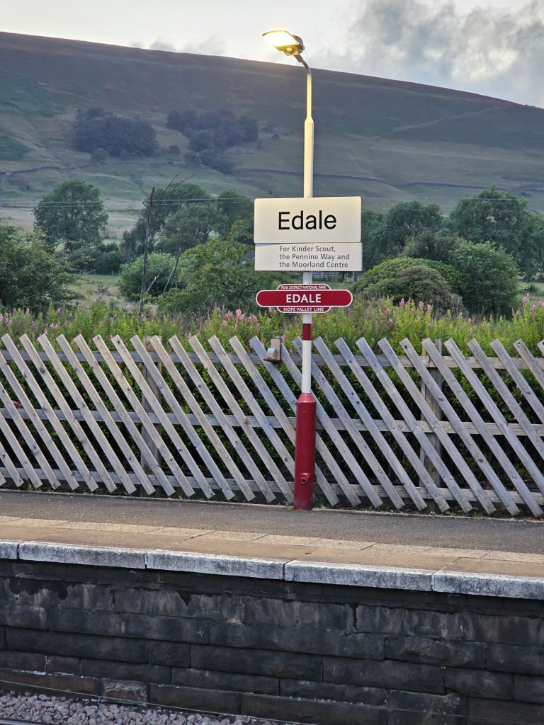 Train station name sign on the platform in Edale, Peak District. A hill can be seen behind it.