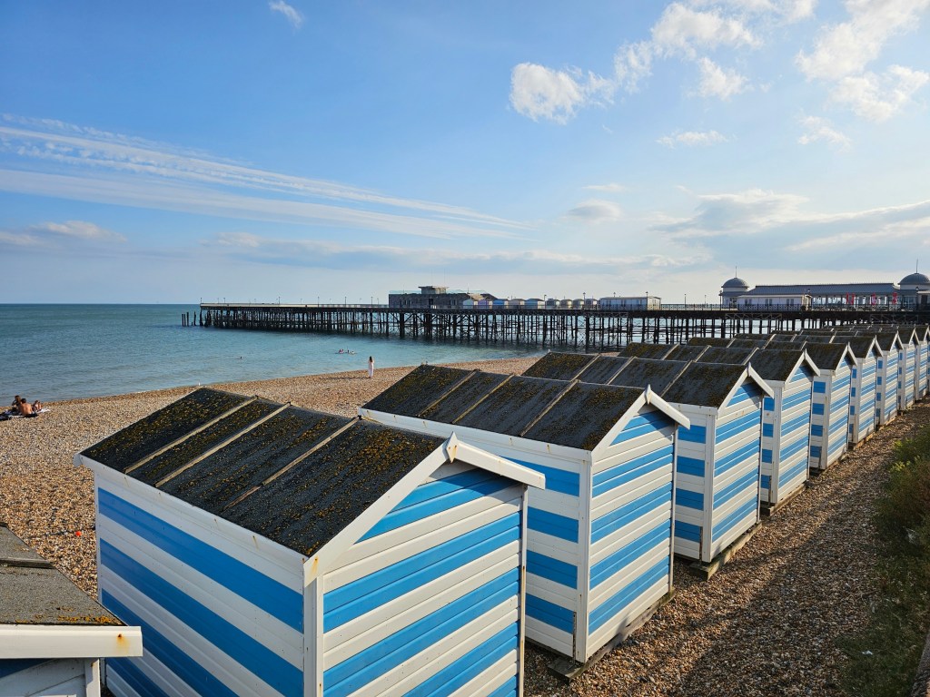 White and blue beach huts and Hastings Pier behind them