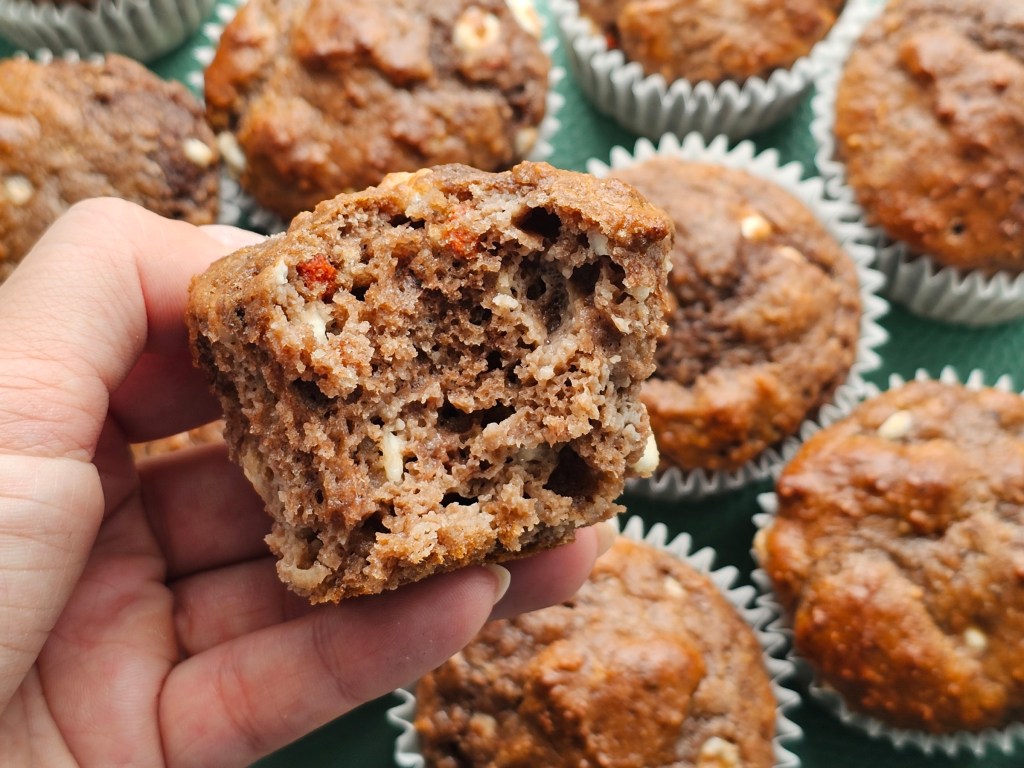 A close up view of baked protein muffins, with a hand holding a halved muffin