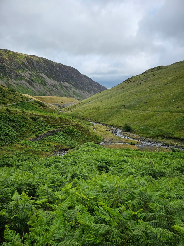 Green hills in a valley between Glenridding and Helvellyn with a small river at the bottom of the valley
