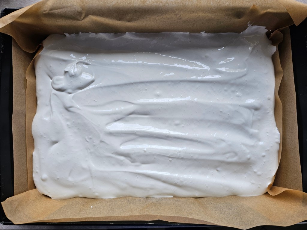 A tray with baked shortbread cake base, a layer of meringue - before baking
